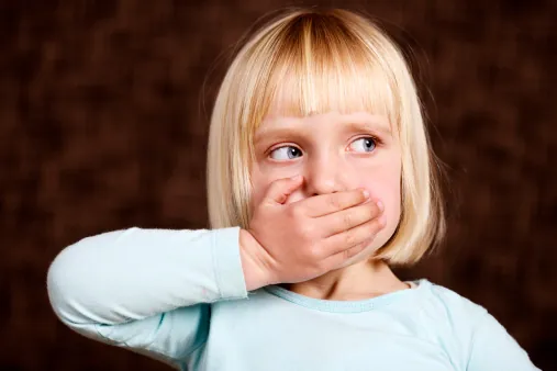A young blonde girl holds a hand over her mouth and looks away to the side