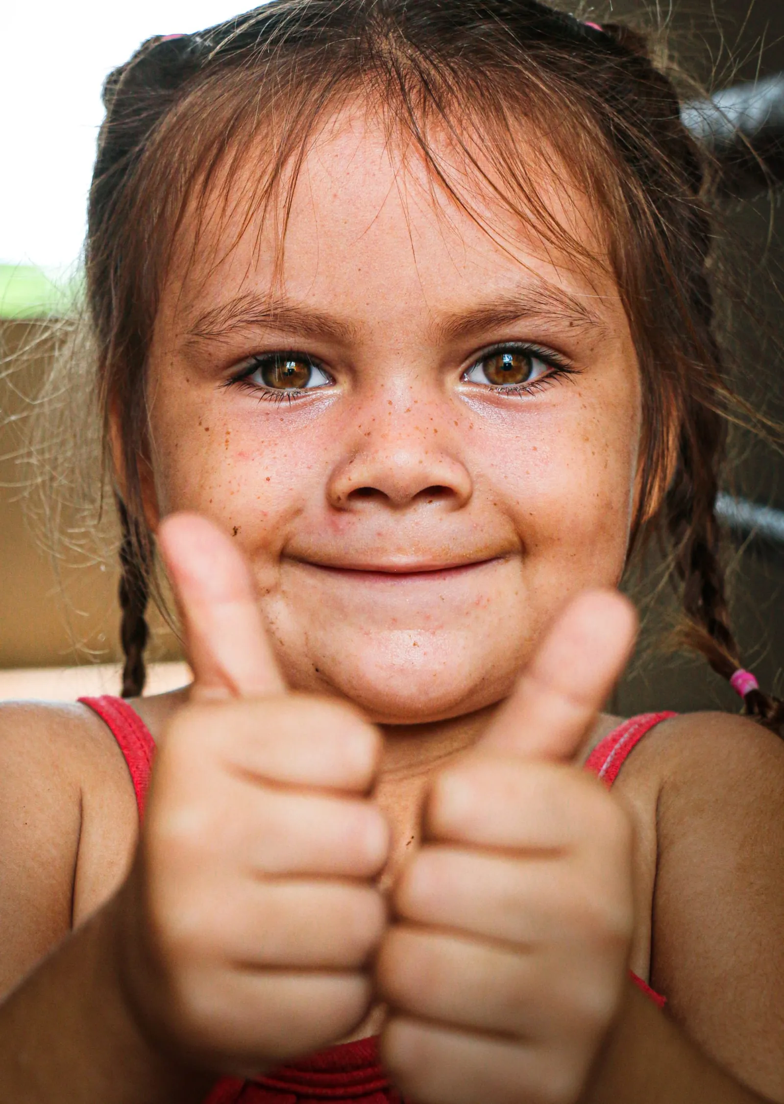 A freckled girl with braids smiles at the camera and gives two thumbs up