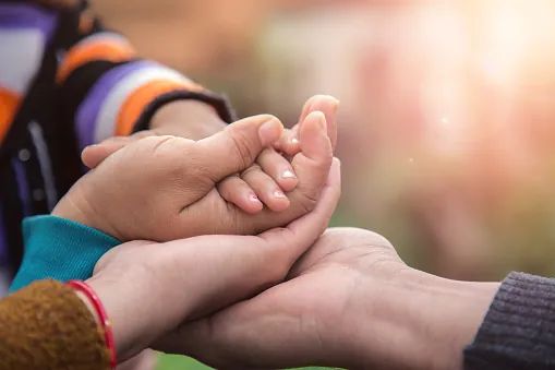 A child's hand resting in two adults' cupped palms, outdoors in warm light